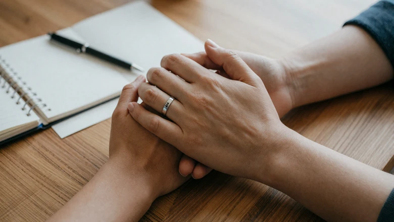 Two hands gently intertwined on a table beside a journal, symbolizing partnership and shared planning in bipolar relationships